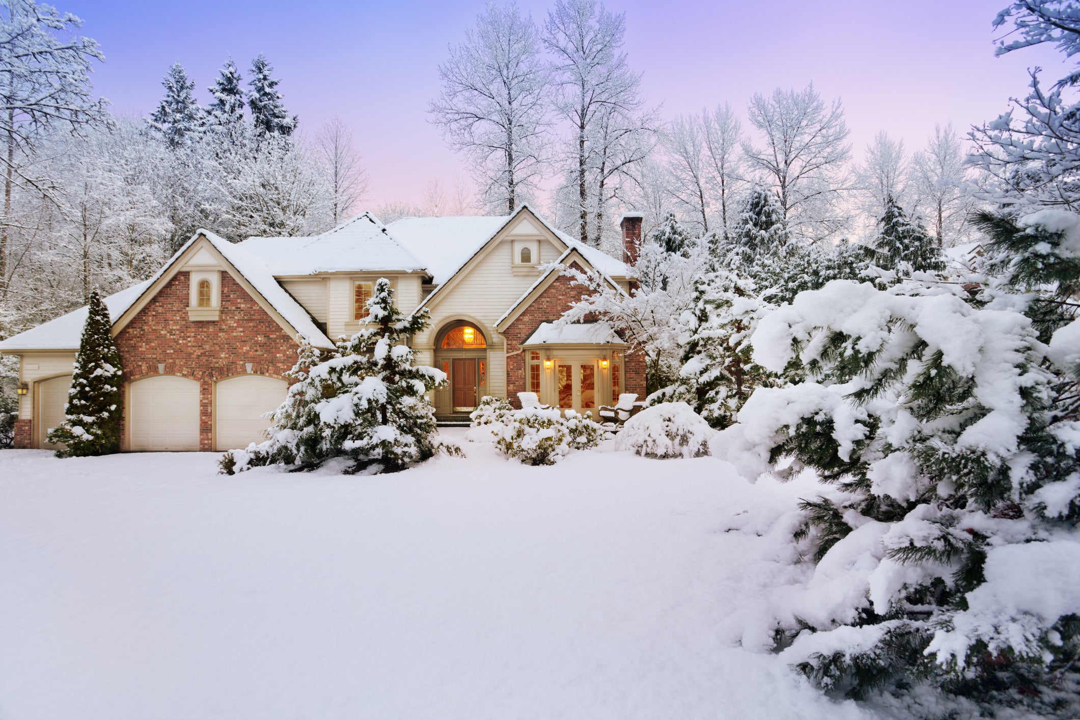 a home is surrounded by fluffy snow with trees in the background