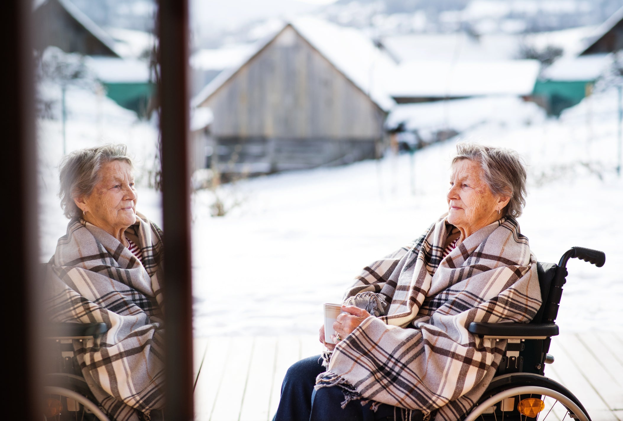 an old woman stares into her reflection while outside in a chilly winter