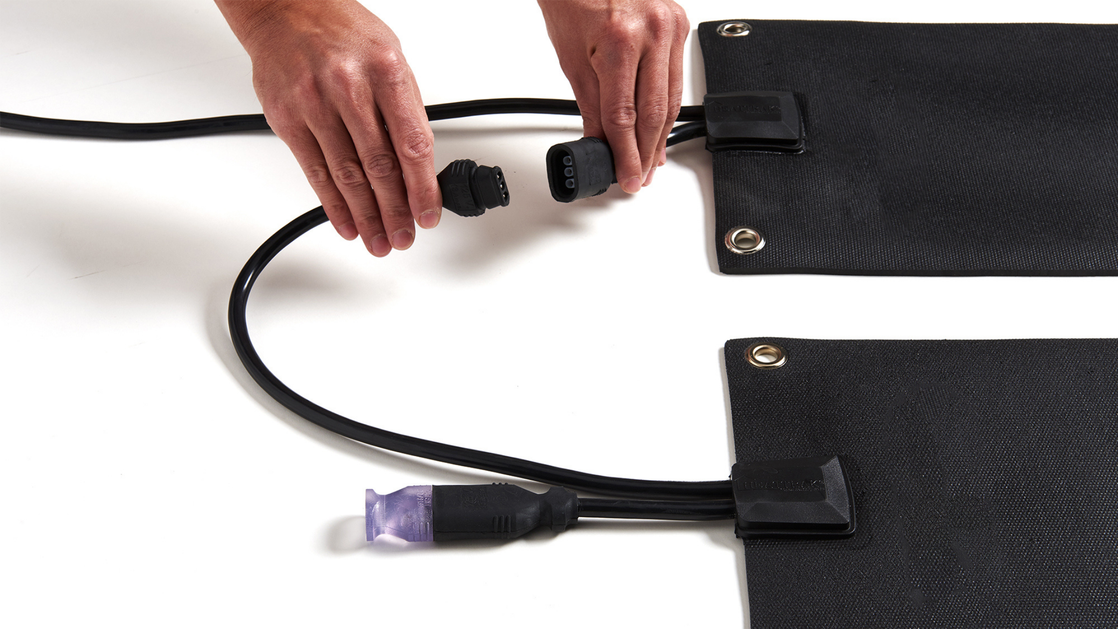 A pair of hands is shown to almost close the connecter cables attached to a pair of HeatTrak stair mats