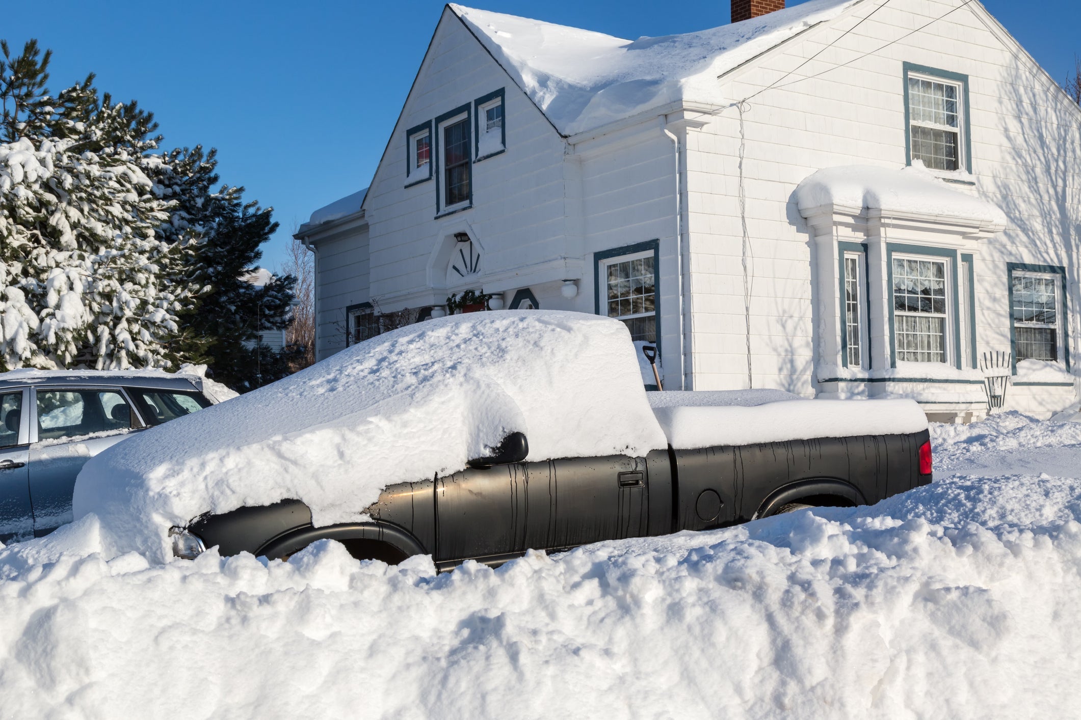 a truck is covered everywhere in snow with a white home in the background