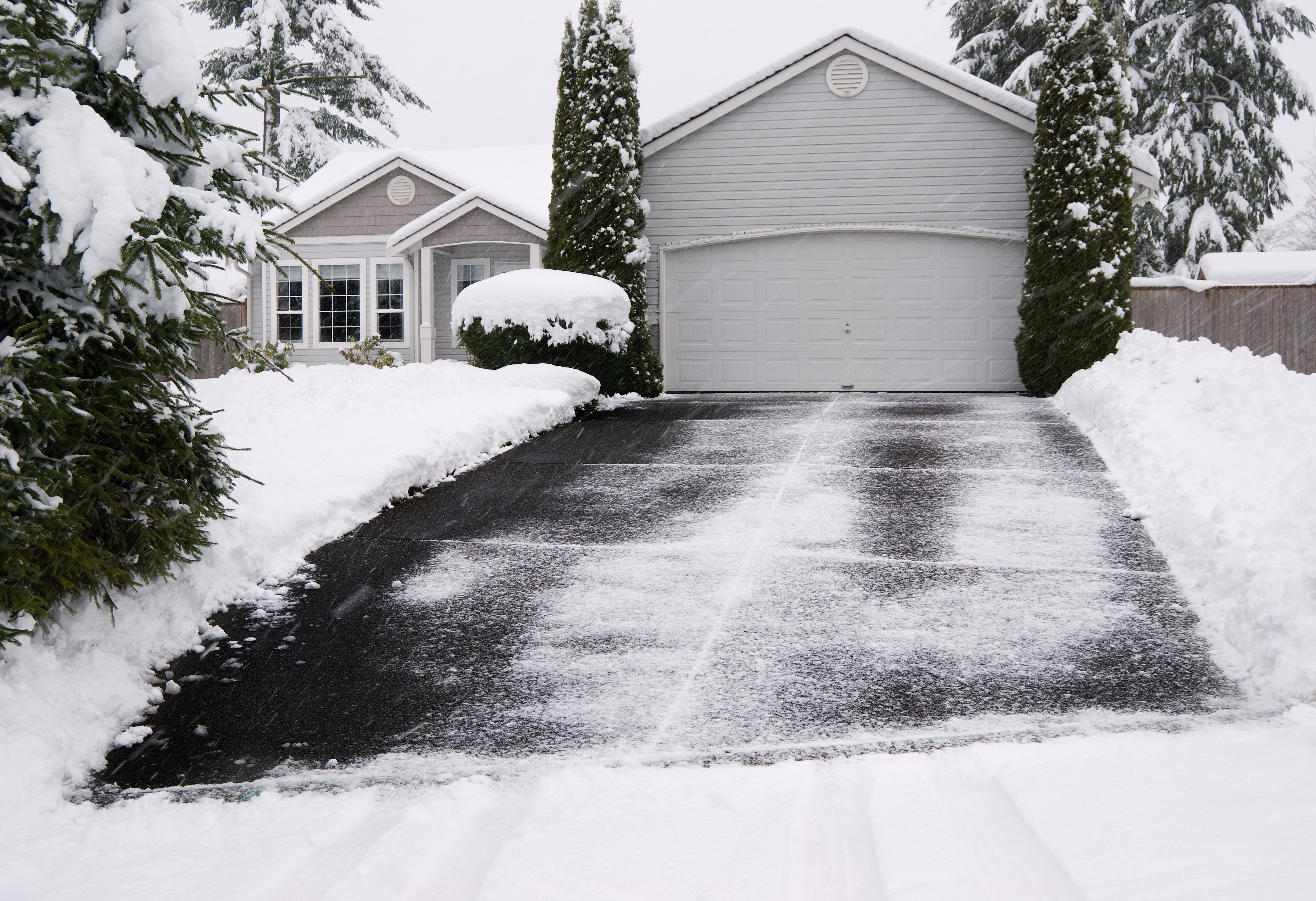a medium sized home is blanketed in snow that features a large driveway surrounded by trees.